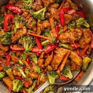 A spoon serves spicy Hunan chicken from a skillet, showing its rich sauce and vegetables.