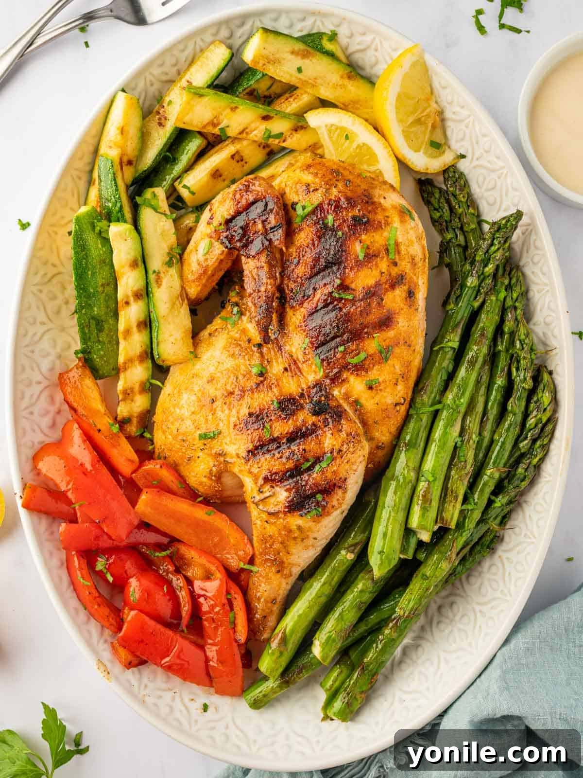 Grilled half chicken on a platter with grilled veggies.