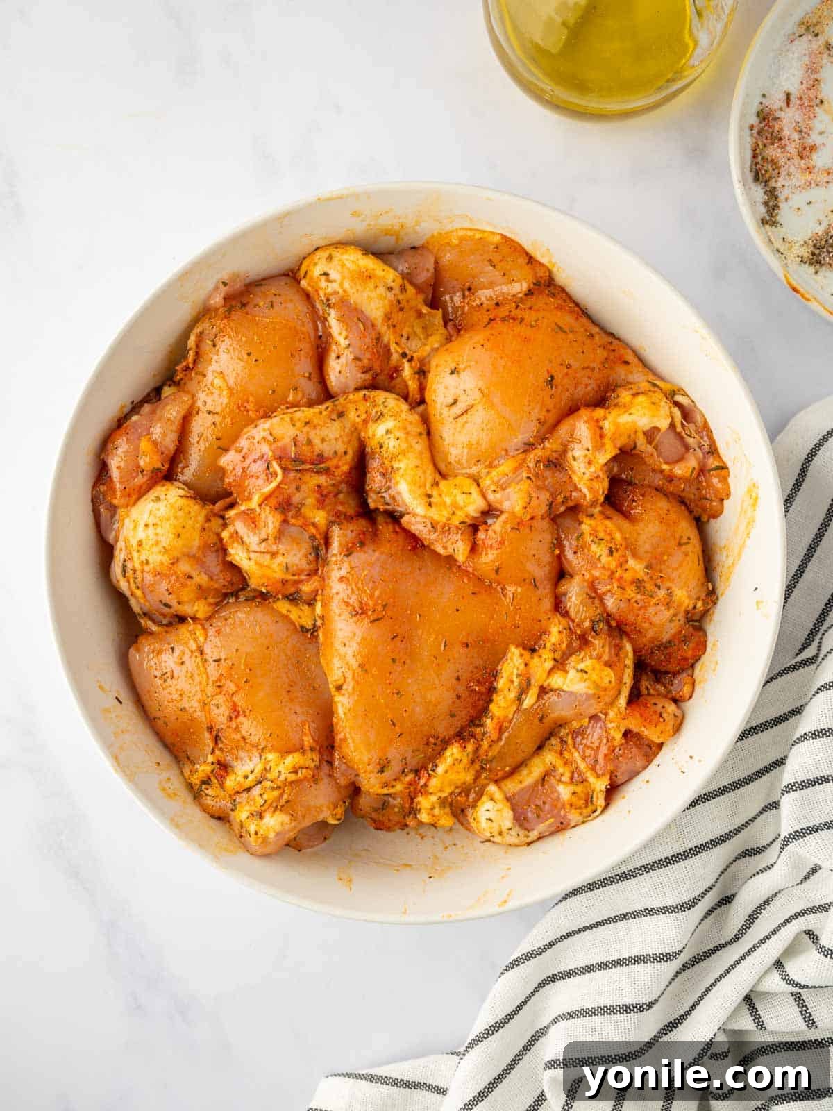 Close-up shot of raw chicken thighs being thoroughly marinated with a savory blend of seasonings and olive oil in a bowl.