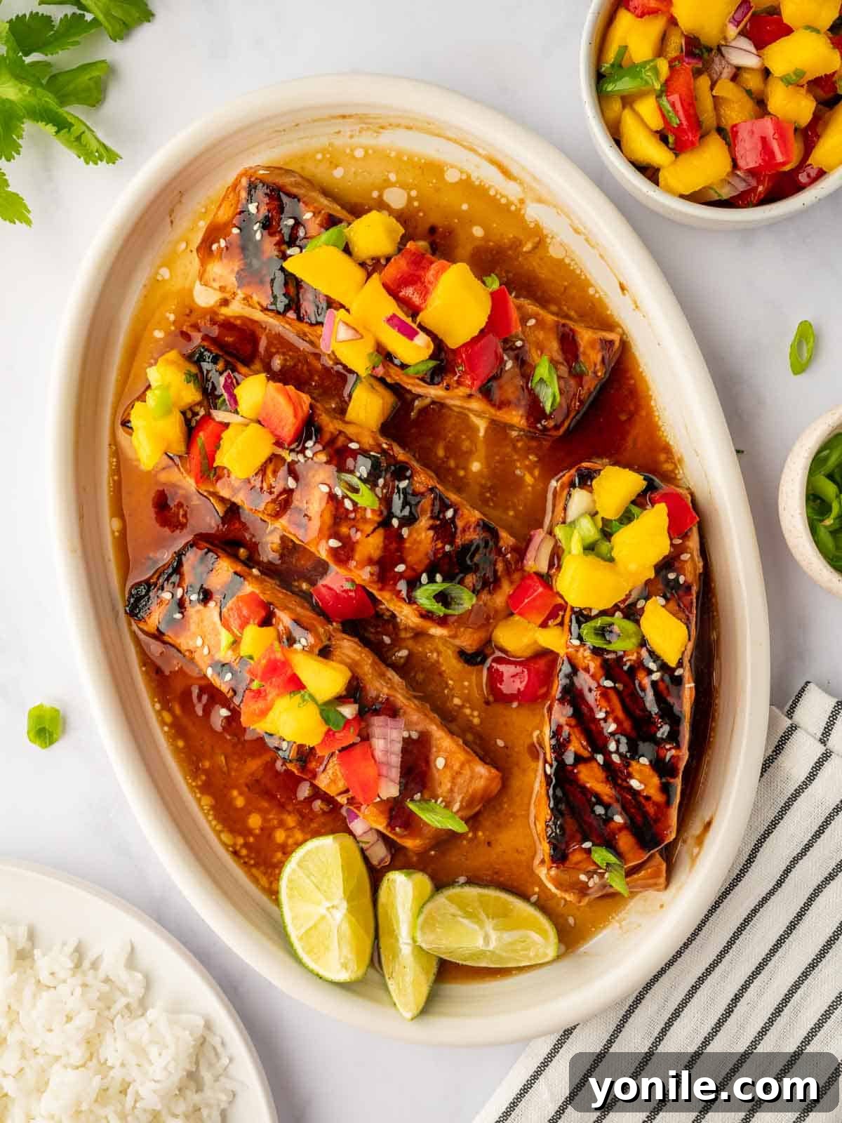 Grilled salmon on a plate topped with fresh mango salsa, garnished with green onions and sesame seeds.