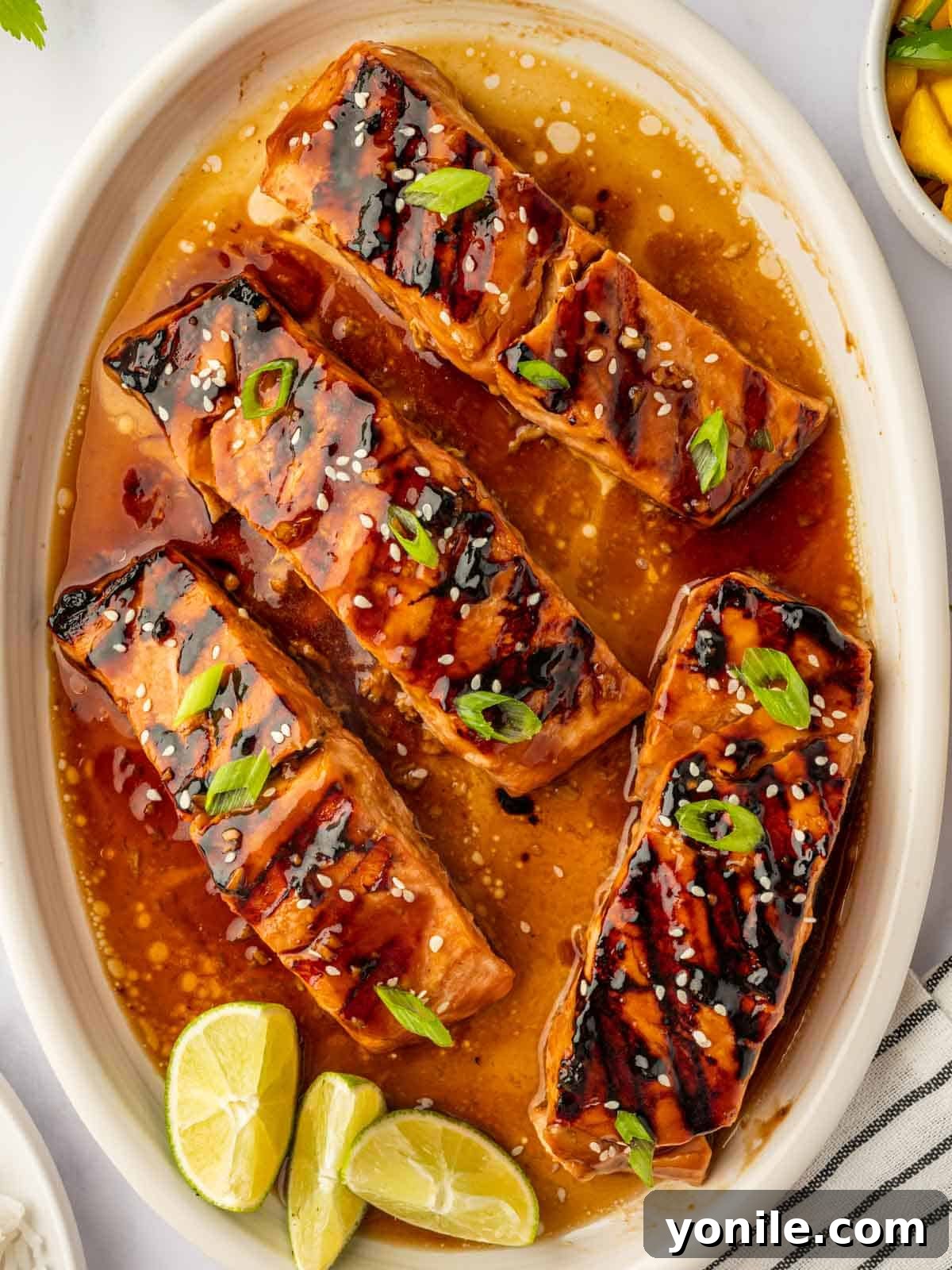 Grilled salmon teriyaki garnished with green onions and sesame seeds on a plate.