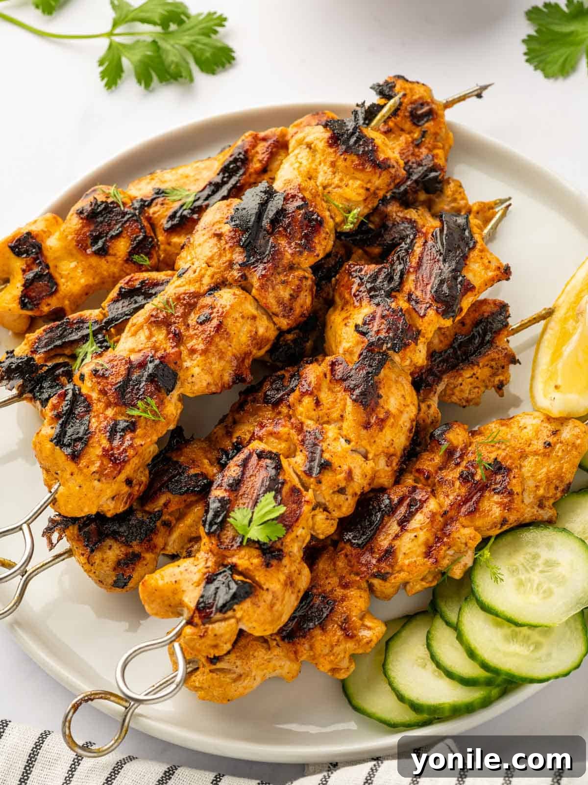 Beautifully grilled Tandoori chicken skewers served on a platter with fresh cucumber slices.
