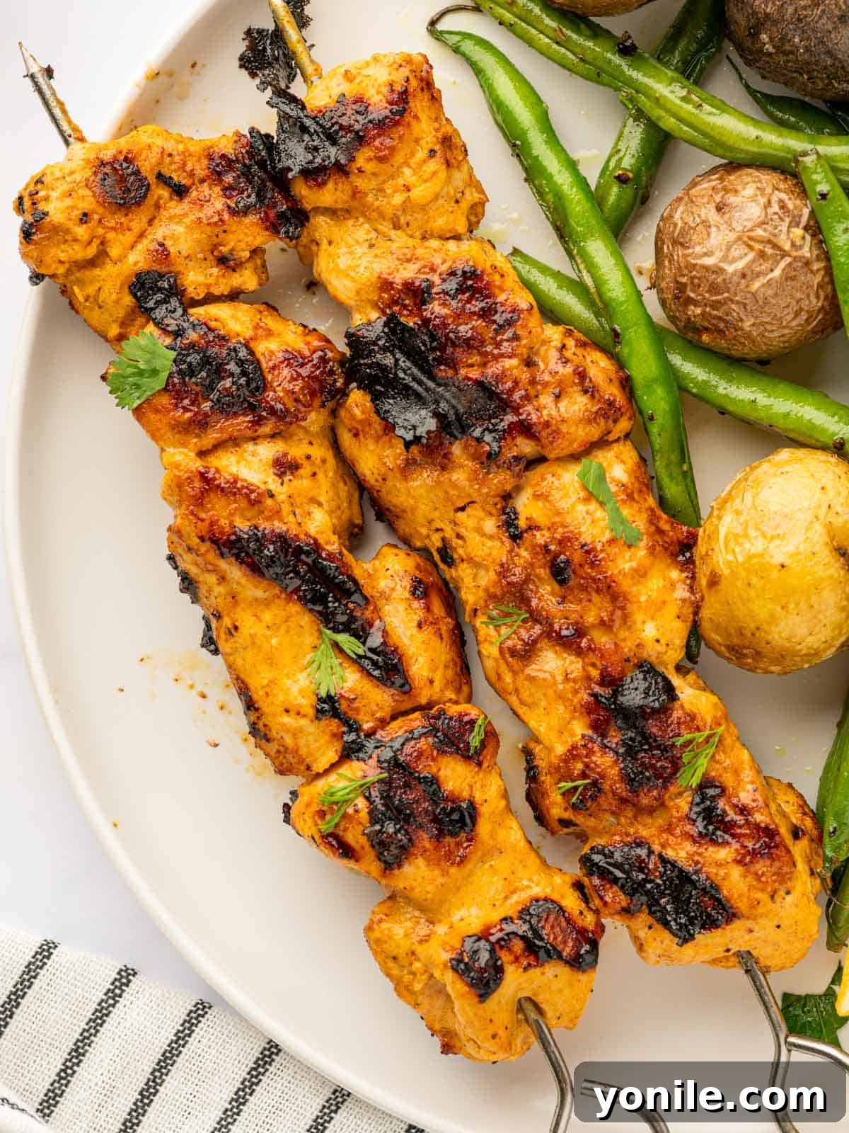 A vibrant plate of Tandoori chicken skewers, accompanied by green beans and roasted potatoes, creating a complete and delicious meal.