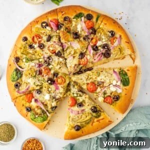 Sliced homemade Mediterranean pizza on a pizza stone, garnished with fresh herbs.