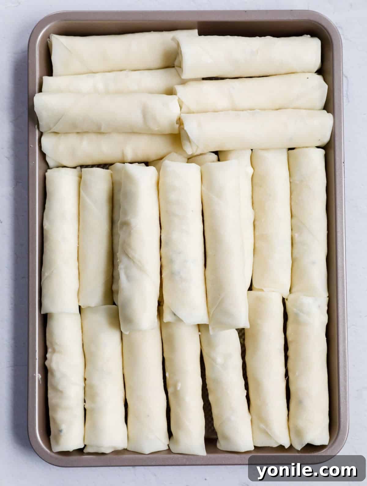 Crispy Cheese Rolls 6 A collection of uncooked cheese rolls meticulously arranged in a frying pan, poised for the deep frying process to achieve their signature golden crispness.
