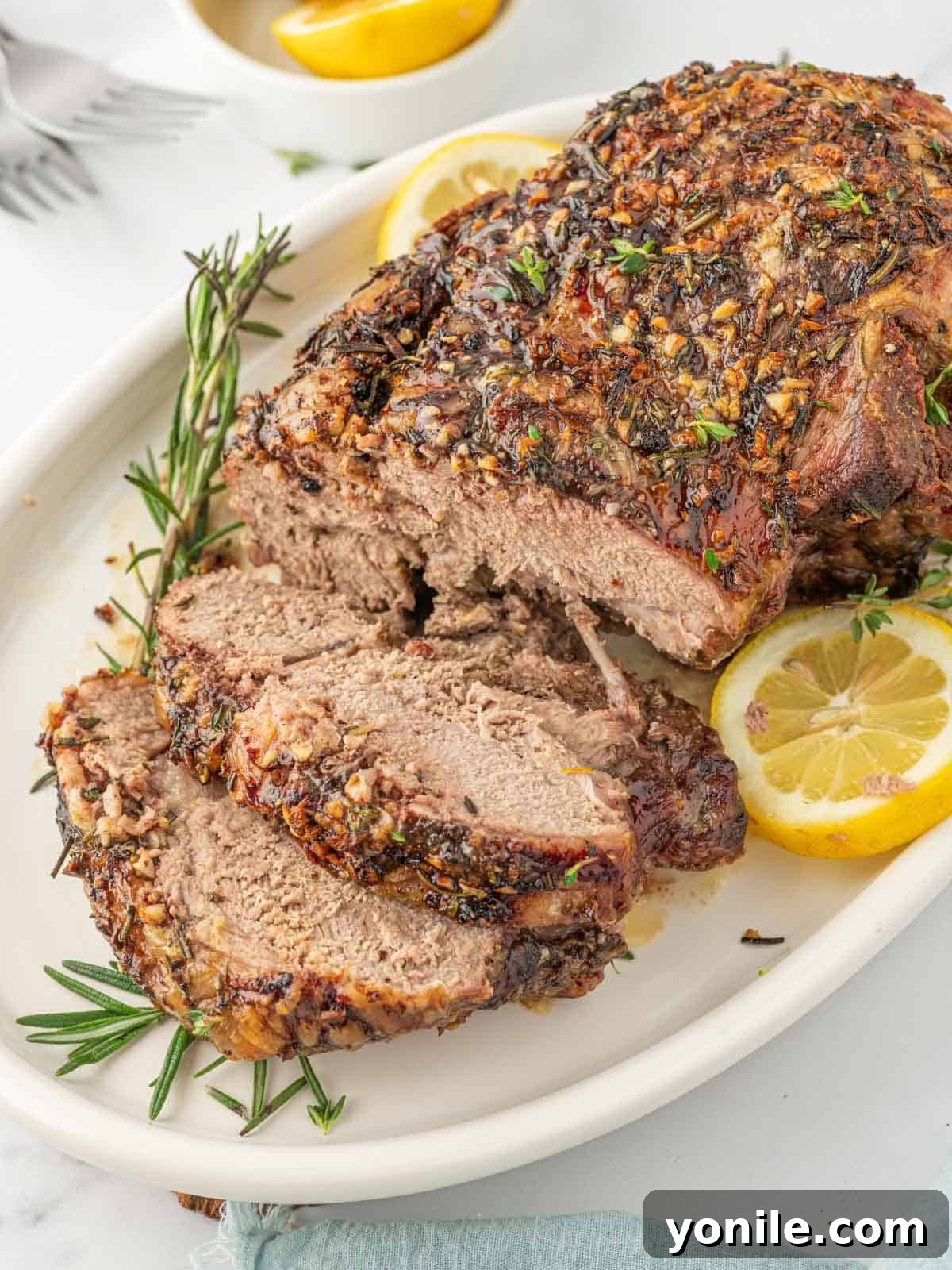 Succulent slices of roasted boneless leg of lamb garnished with fresh lemon wedges and rosemary sprigs, presented elegantly for serving.