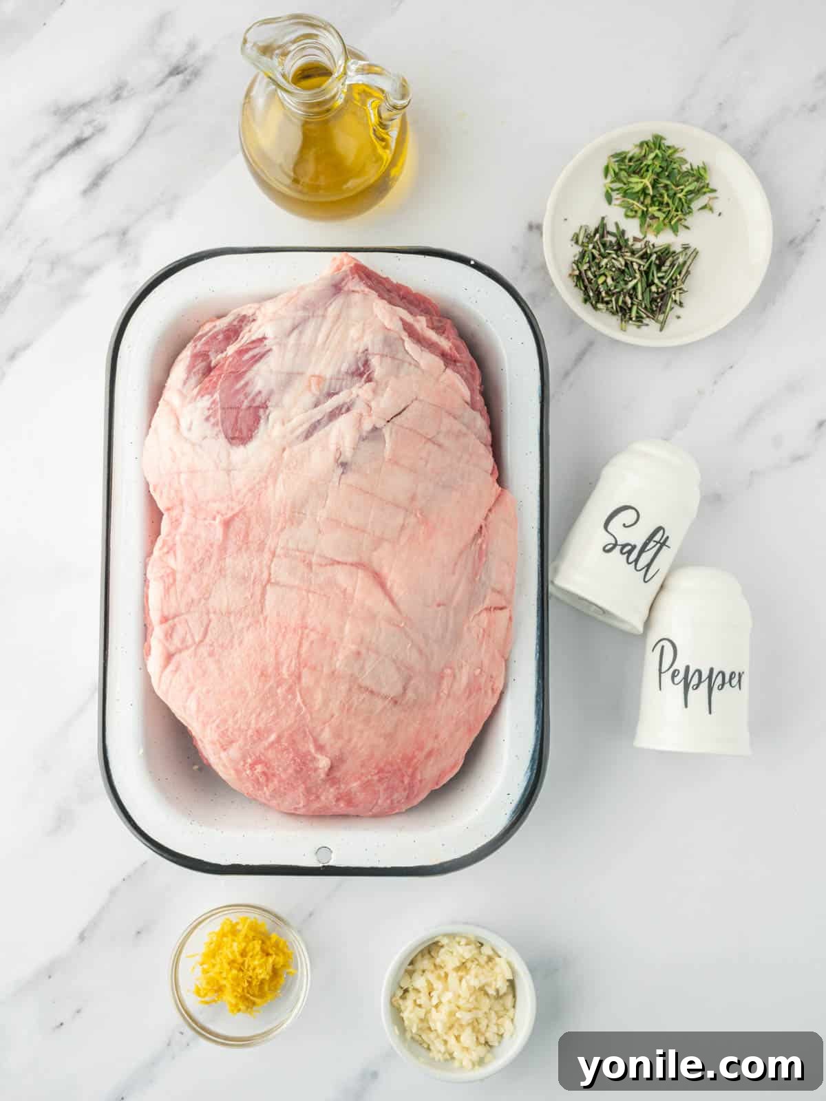 A vibrant assortment of fresh ingredients including whole garlic cloves, a bright lemon, sprigs of rosemary, and a bottle of olive oil, all laid out for the roasted garlic lamb recipe.