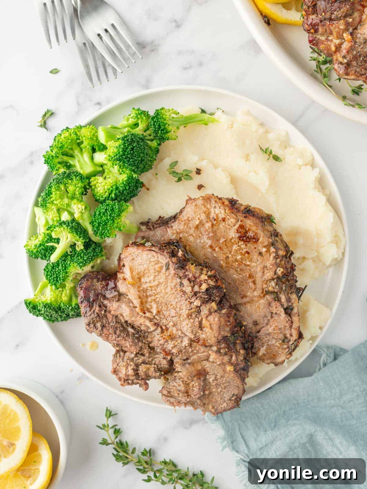 A festive dining plate featuring elegant slices of roasted lamb, accompanied by a generous scoop of creamy mashed potatoes and vibrant green broccoli florets, creating a complete and appealing meal.