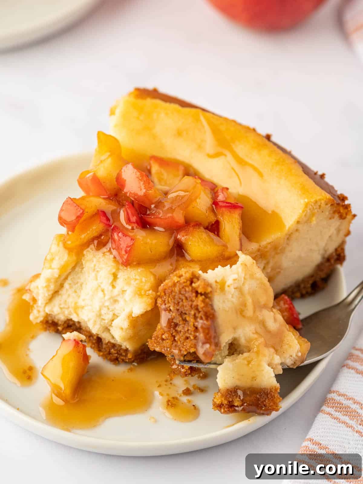 A fork taking a bite from a slice of creamy cinnamon apple cheesecake, showing the texture and topping.