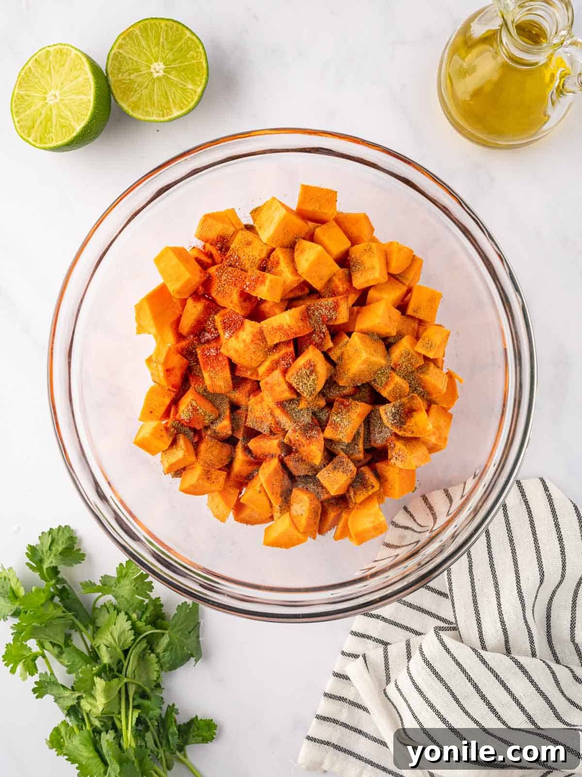 Close-up of sweet potato cubes seasoned with spices in a mixing bowl.