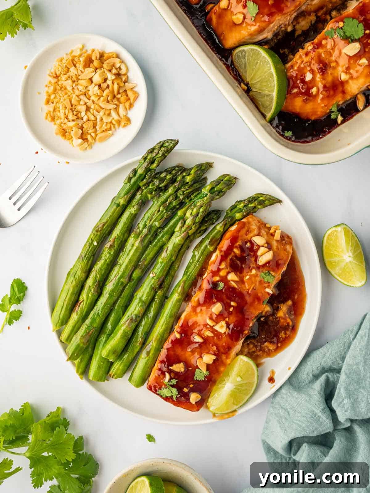 Thai Chili-Lime Baked Salmon 2 Perfectly baked Thai salmon on a plate, garnished with fresh herbs and served alongside tender asparagus spears.