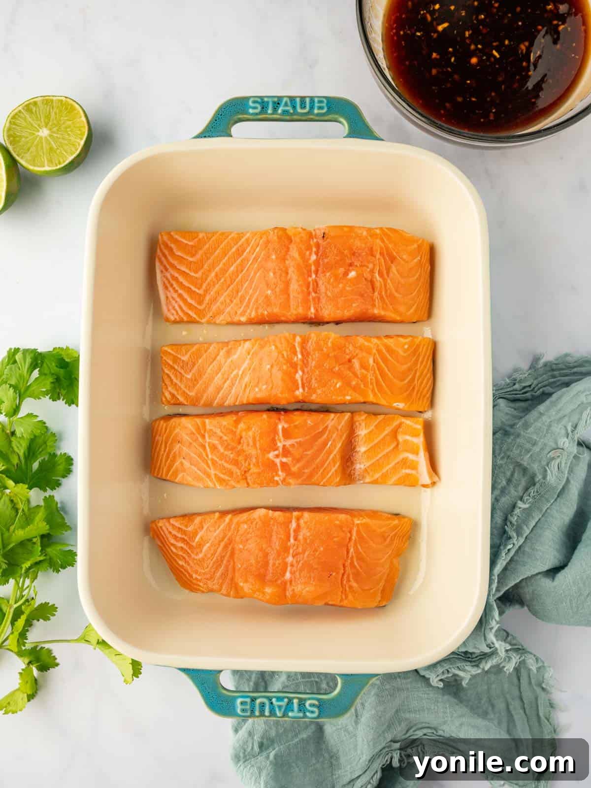 Thai Chili-Lime Baked Salmon 4 Fresh salmon fillets neatly arranged in a baking dish, ready to be seasoned and marinated for a delicious meal.