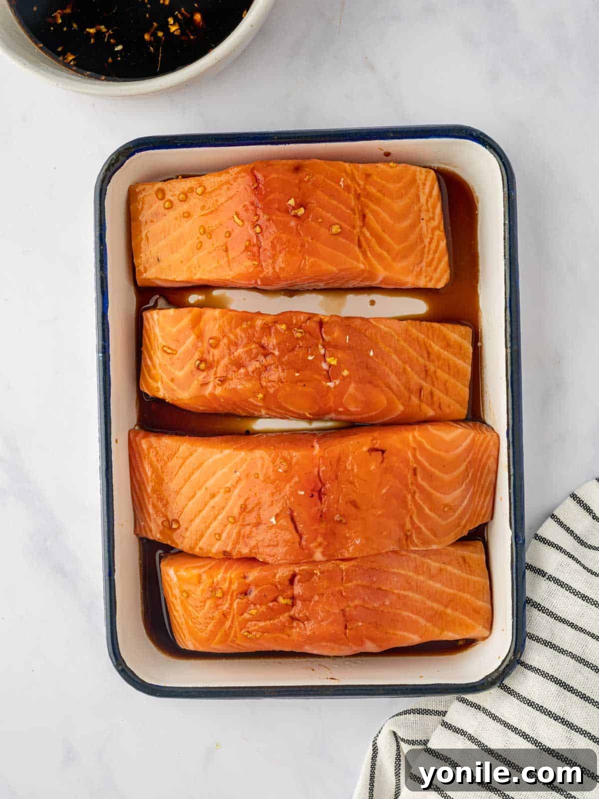 Salmon fillets soaking in a rich, dark teriyaki marinade in a glass dish, absorbing all the savory-sweet flavors.