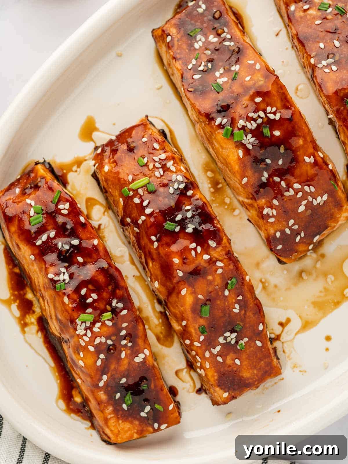 Two perfectly cooked salmon fillets resting on a white plate, glistening with teriyaki glaze, ready to be served.