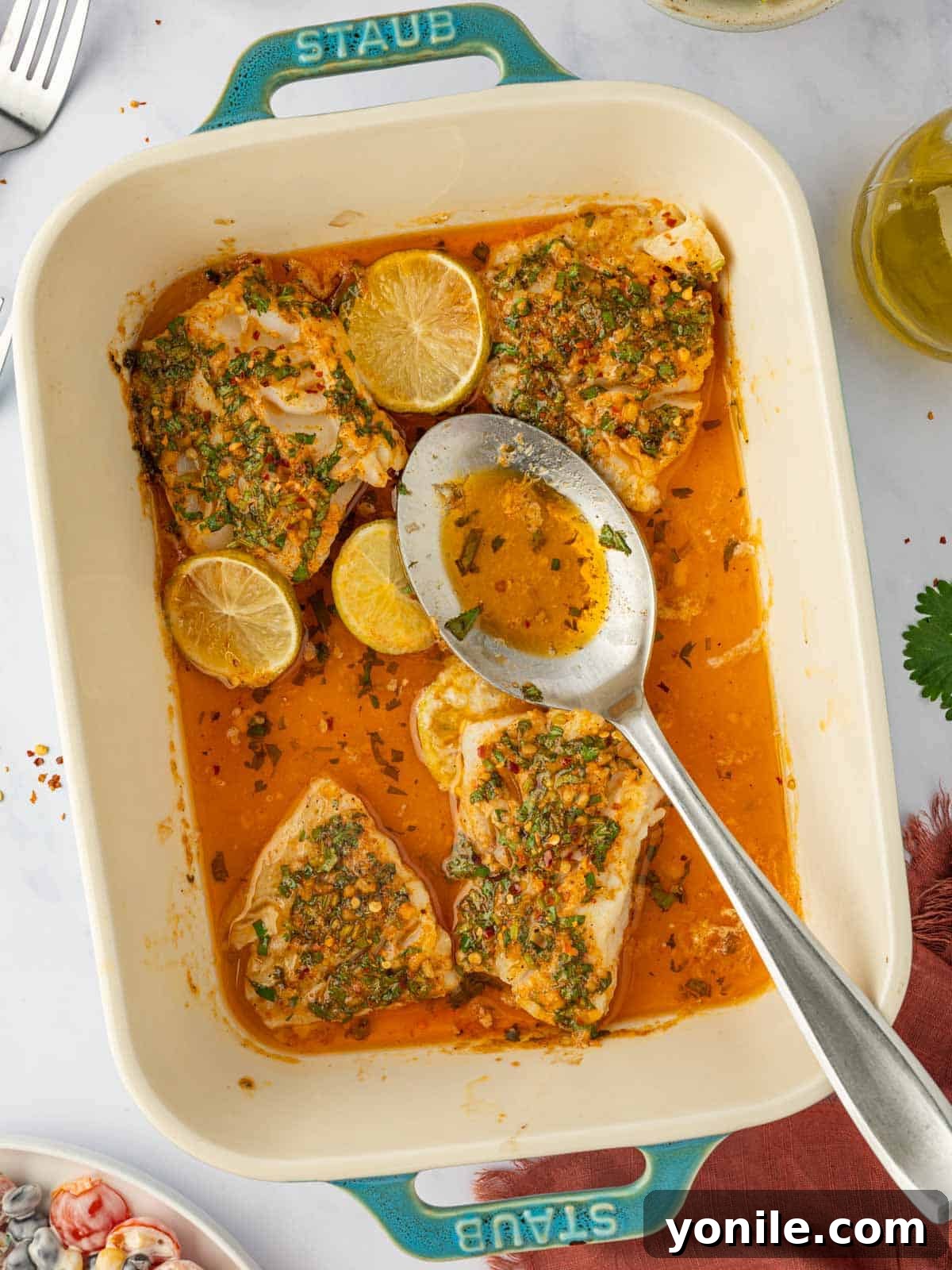 Savory Herb Crusted Cod Bake 8 A spoon ladles rich buttery herb lime cod marinade over cooked fish in a casserole dish.