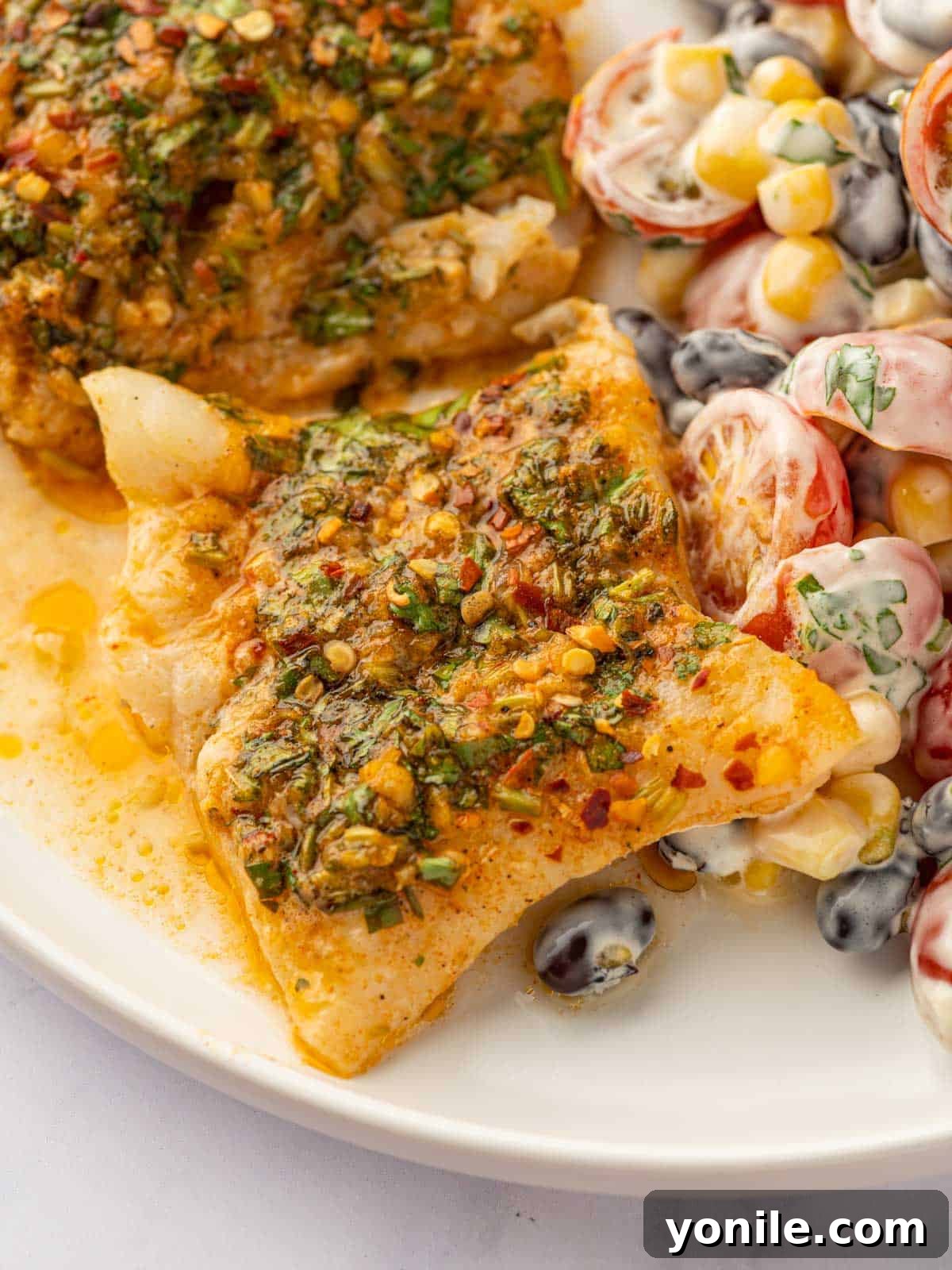 Savory Herb Crusted Cod Bake 9 A simple cod recipe served on a white plate with a fresh tomato salad on the side.