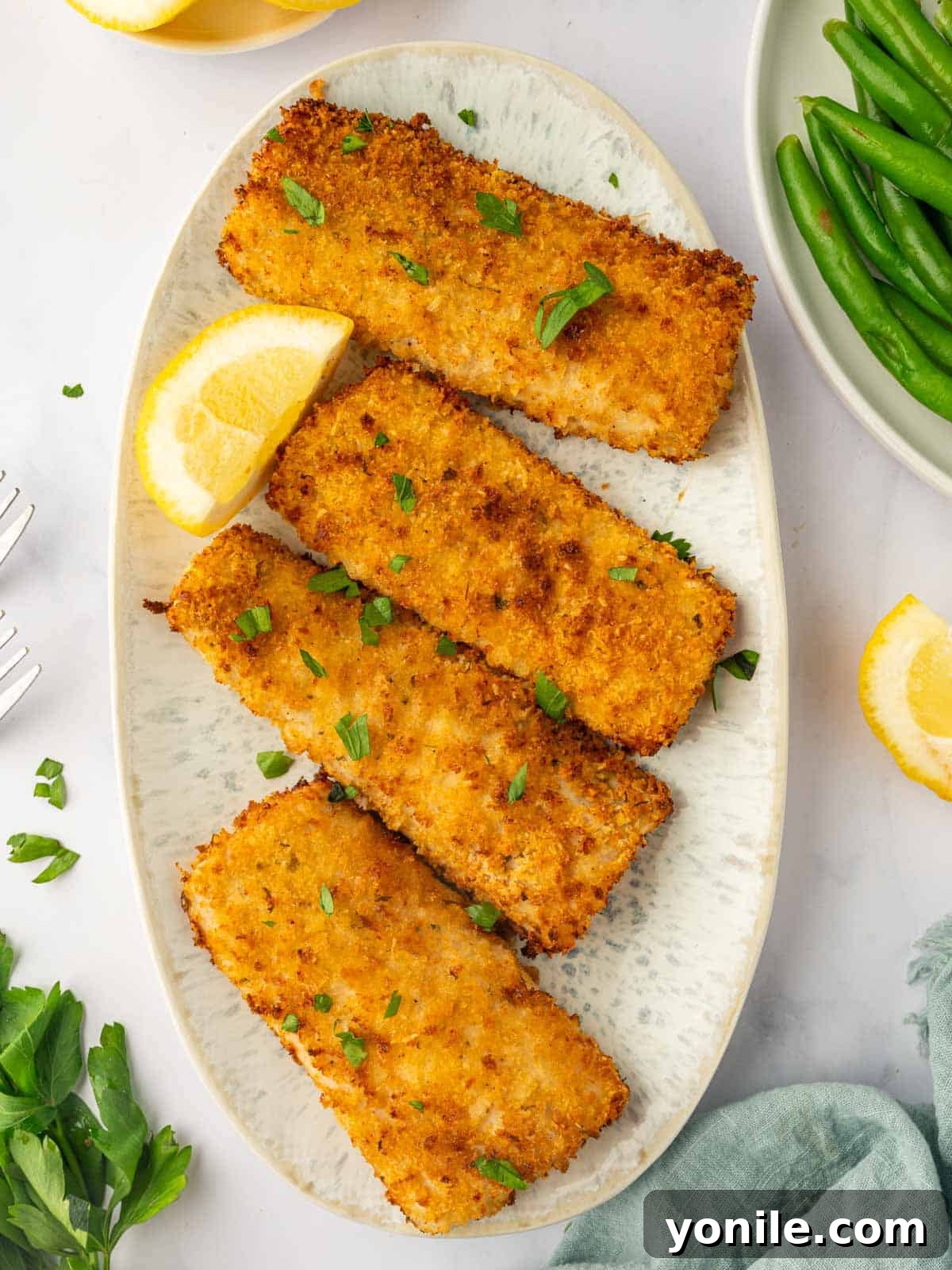 Four pieces of air-fried crispy mahi mahi fish served on a platter with fresh lemon wedges and garnished with vibrant green parsley.