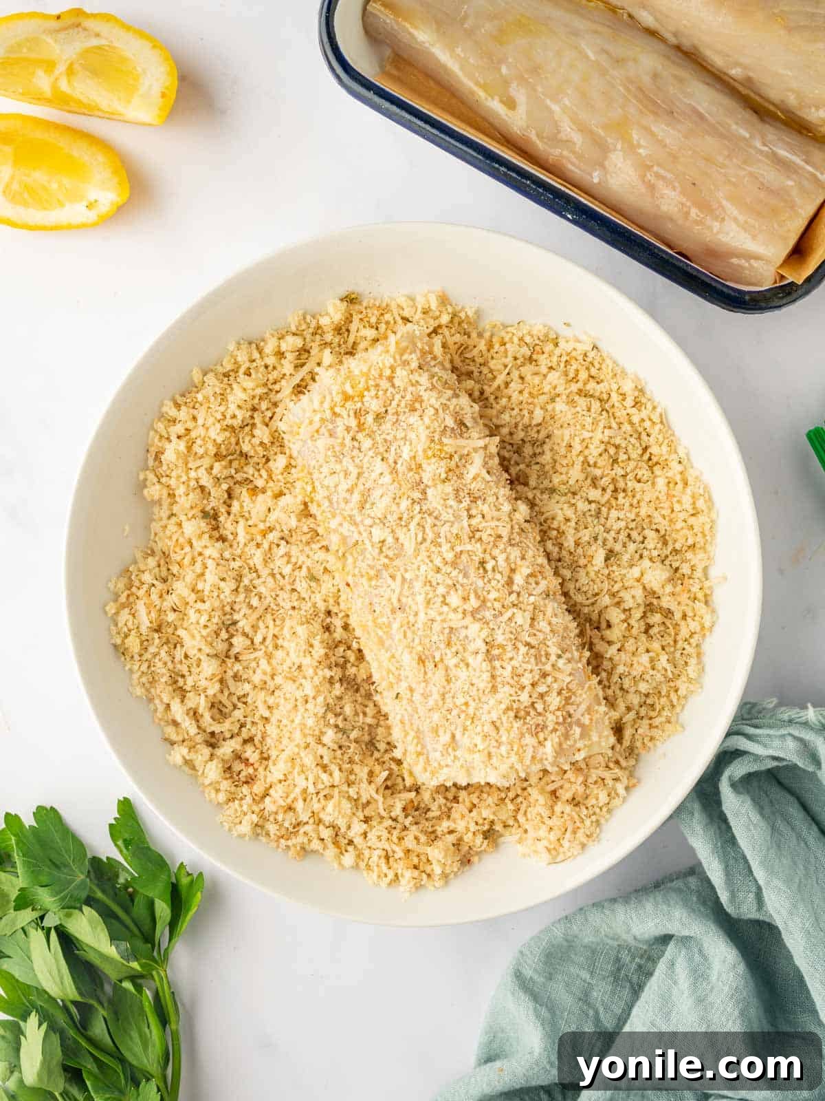 A mahi mahi fish fillet being coated evenly with the panko breadcrumbs and spice mixture in a wide bowl.