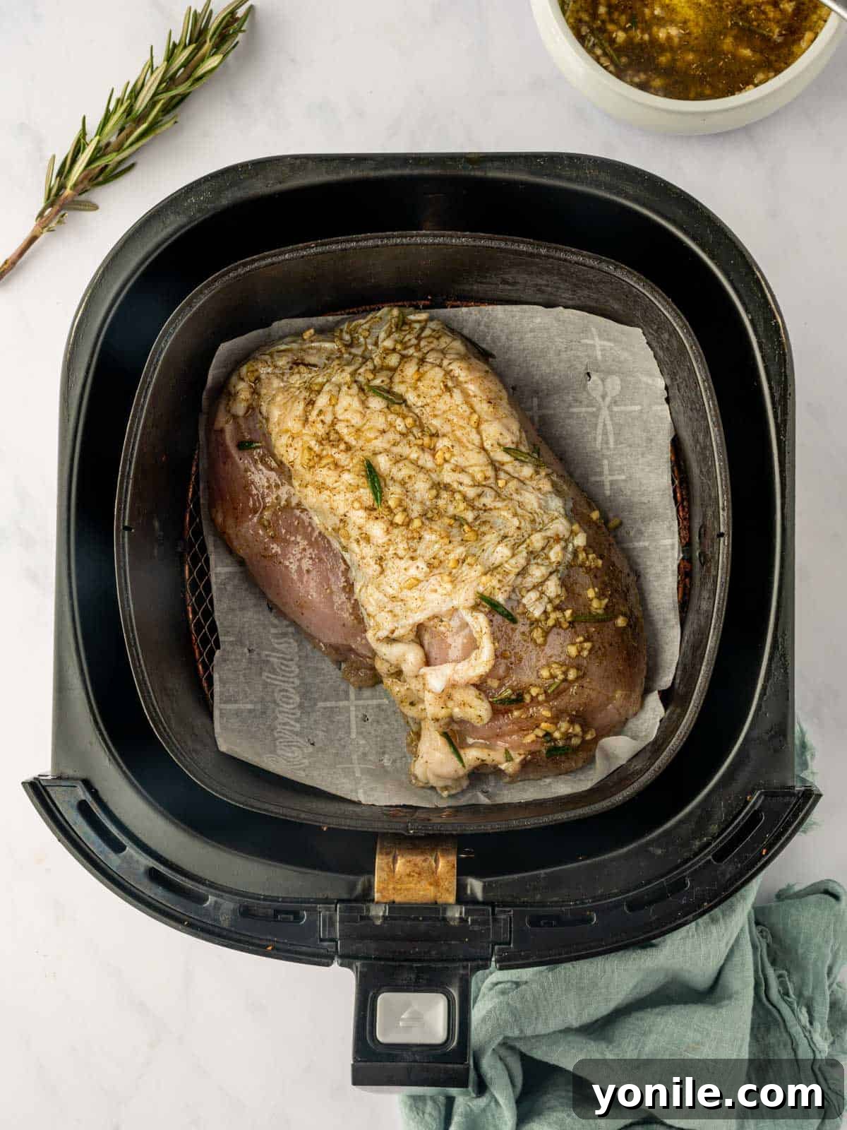 A boneless turkey breast, generously seasoned and placed in an air fryer basket, ready for cooking.