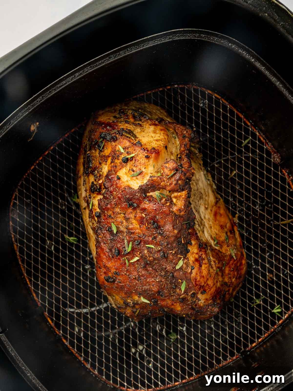 A whole air-fried turkey breast, cooked to a perfect golden brown, resting in the air fryer basket.