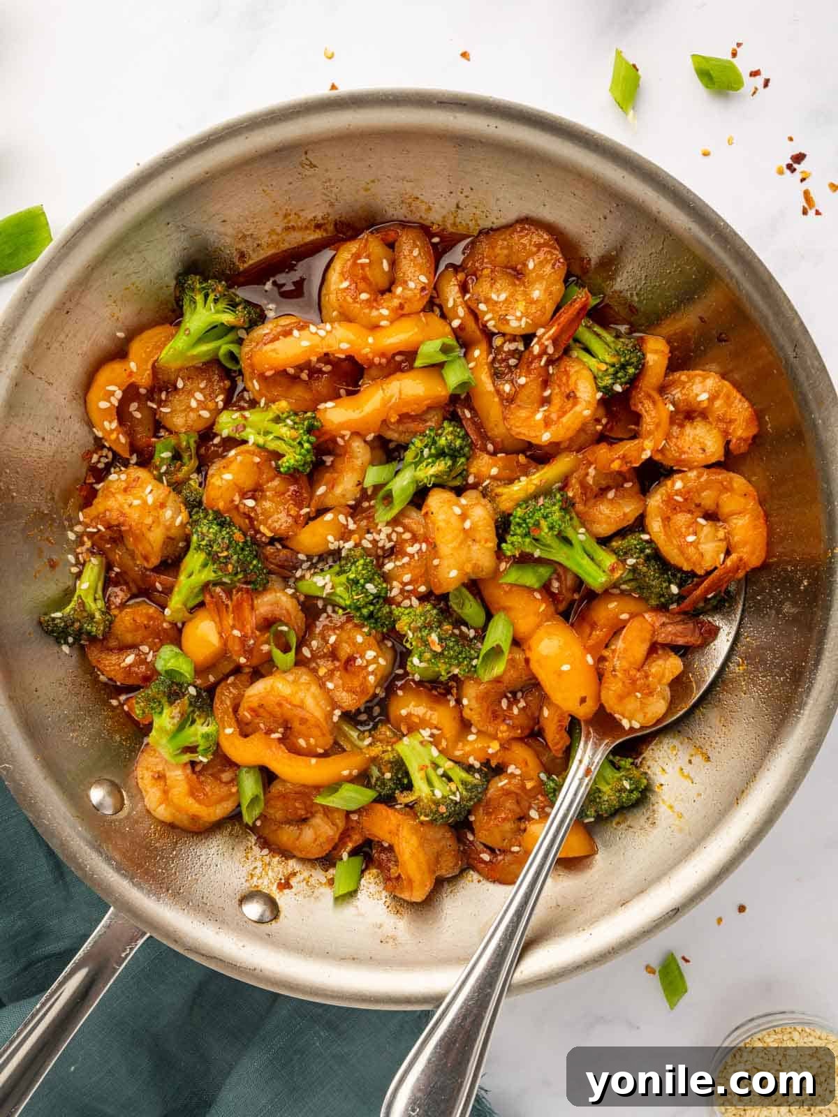 Sticky Sweet Chili Glazed Shrimp 8 A hand stirring cooked shrimp into a glossy sweet chili sauce in a skillet.
