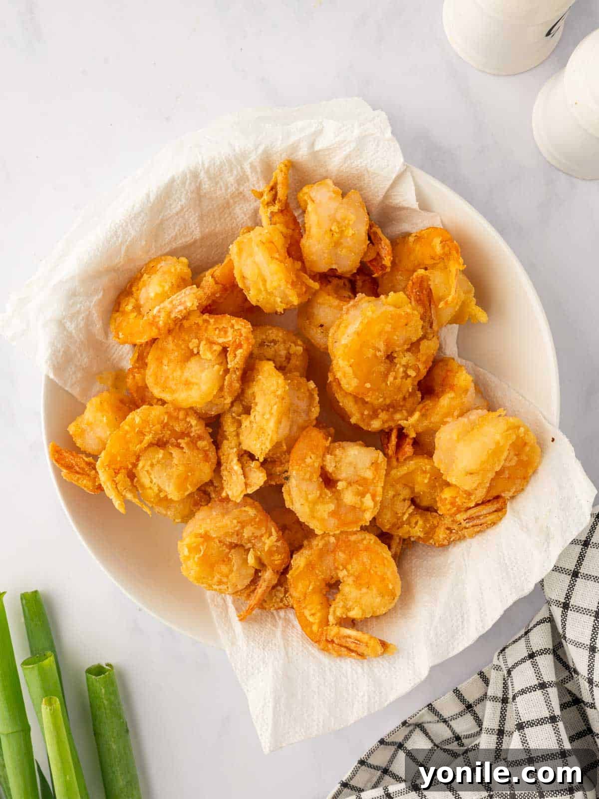 Crispy fried shrimp draining on paper towels to remove excess oil.