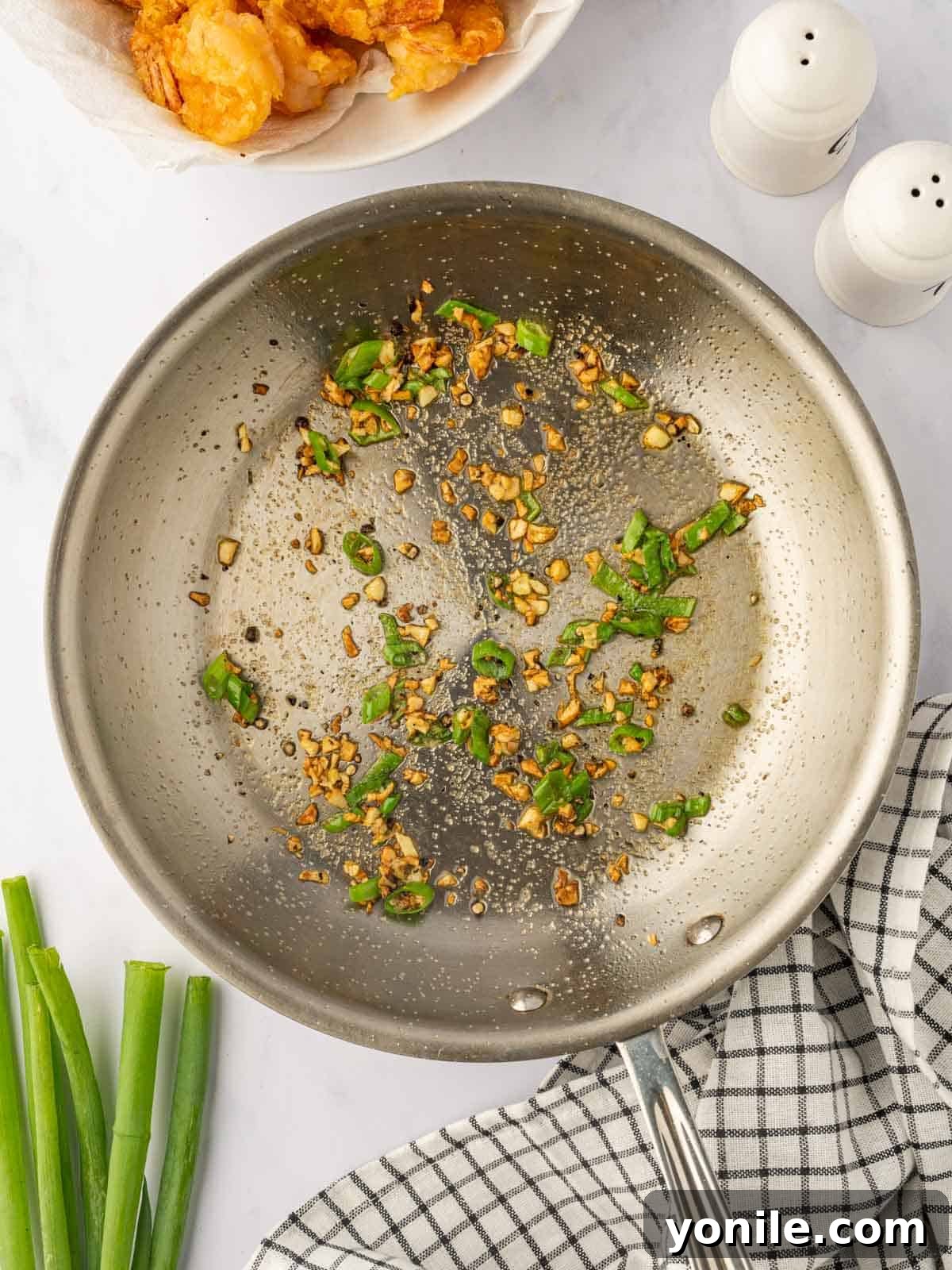 Garlic and green onions being sautéed with seasoning in a skillet.