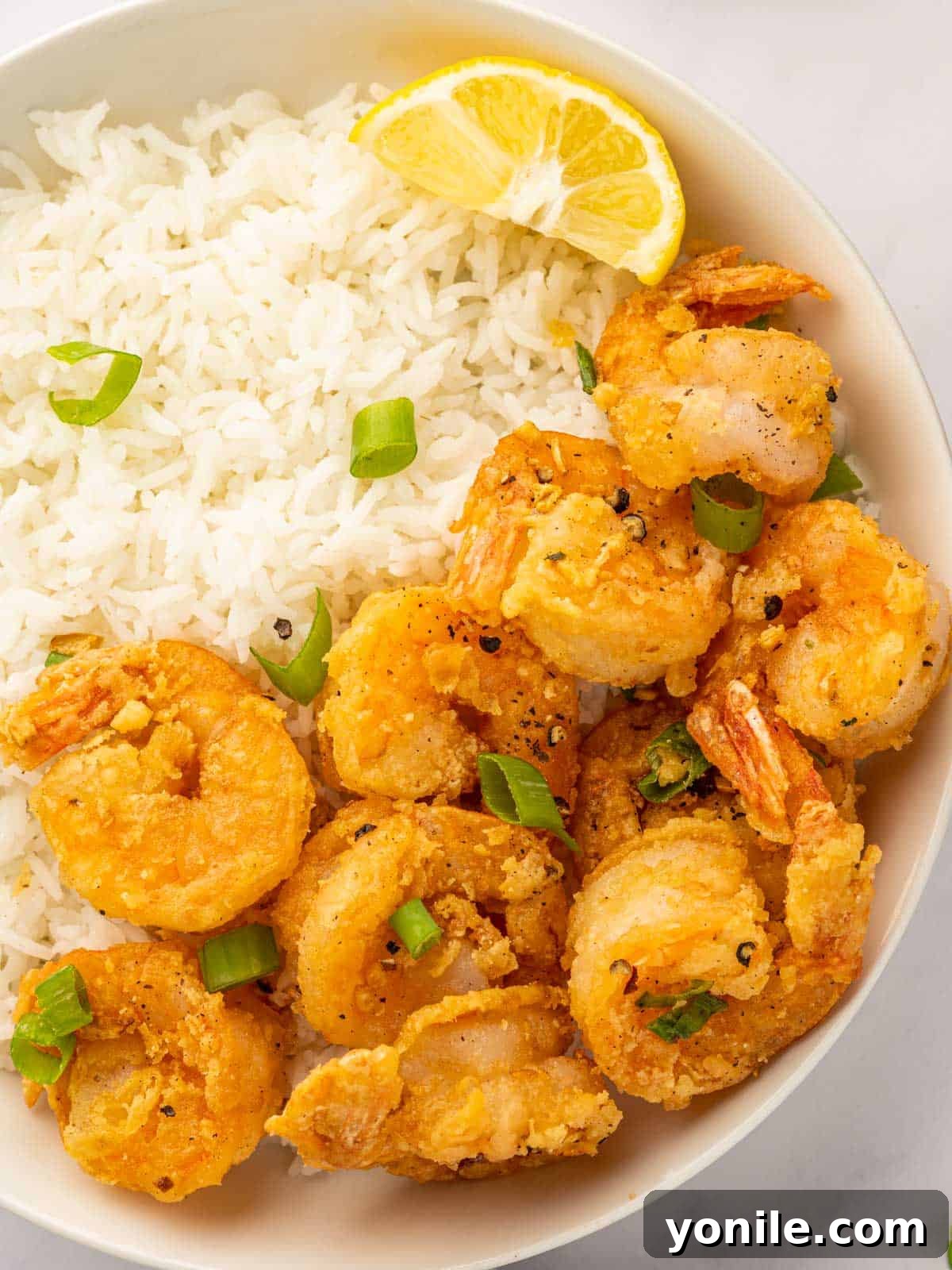 Crispy salt and pepper shrimp served with fluffy white rice on a plate, garnished with green onions.