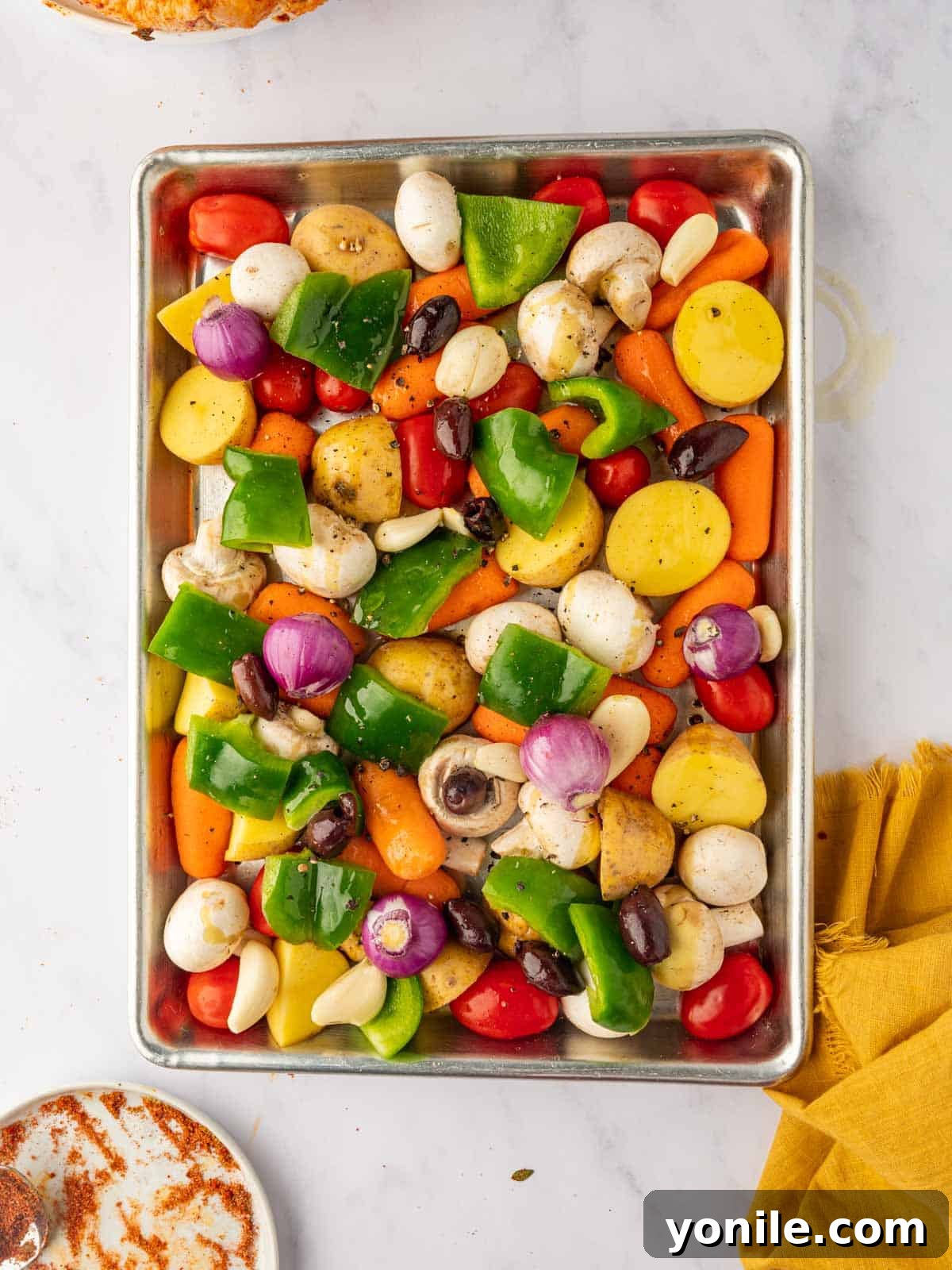 Various chopped vegetables, including potatoes, tomatoes, mushrooms, and bell peppers, neatly arranged on a sheet pan, ready for seasoning.