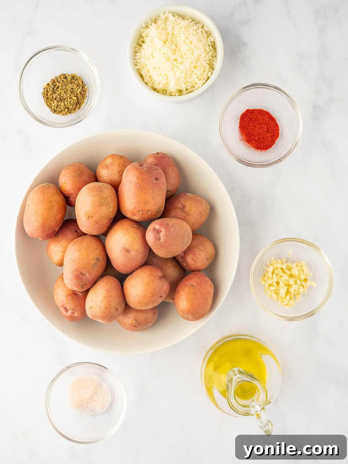 A collection of fresh red potatoes, olive oil, minced garlic, oregano, paprika, salt, pepper, and Parmesan cheese, laid out as ingredients for air fryer red potatoes.
