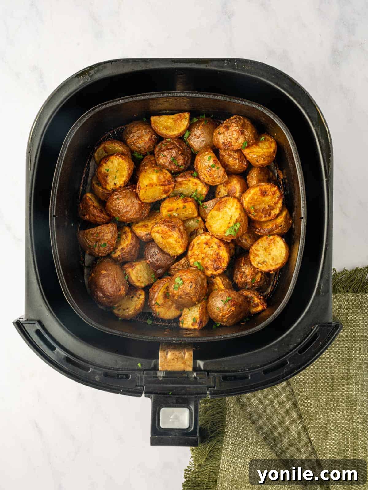 Golden-brown air fried red potatoes are displayed in a serving bowl, garnished with fresh chopped parsley, ready to be enjoyed.