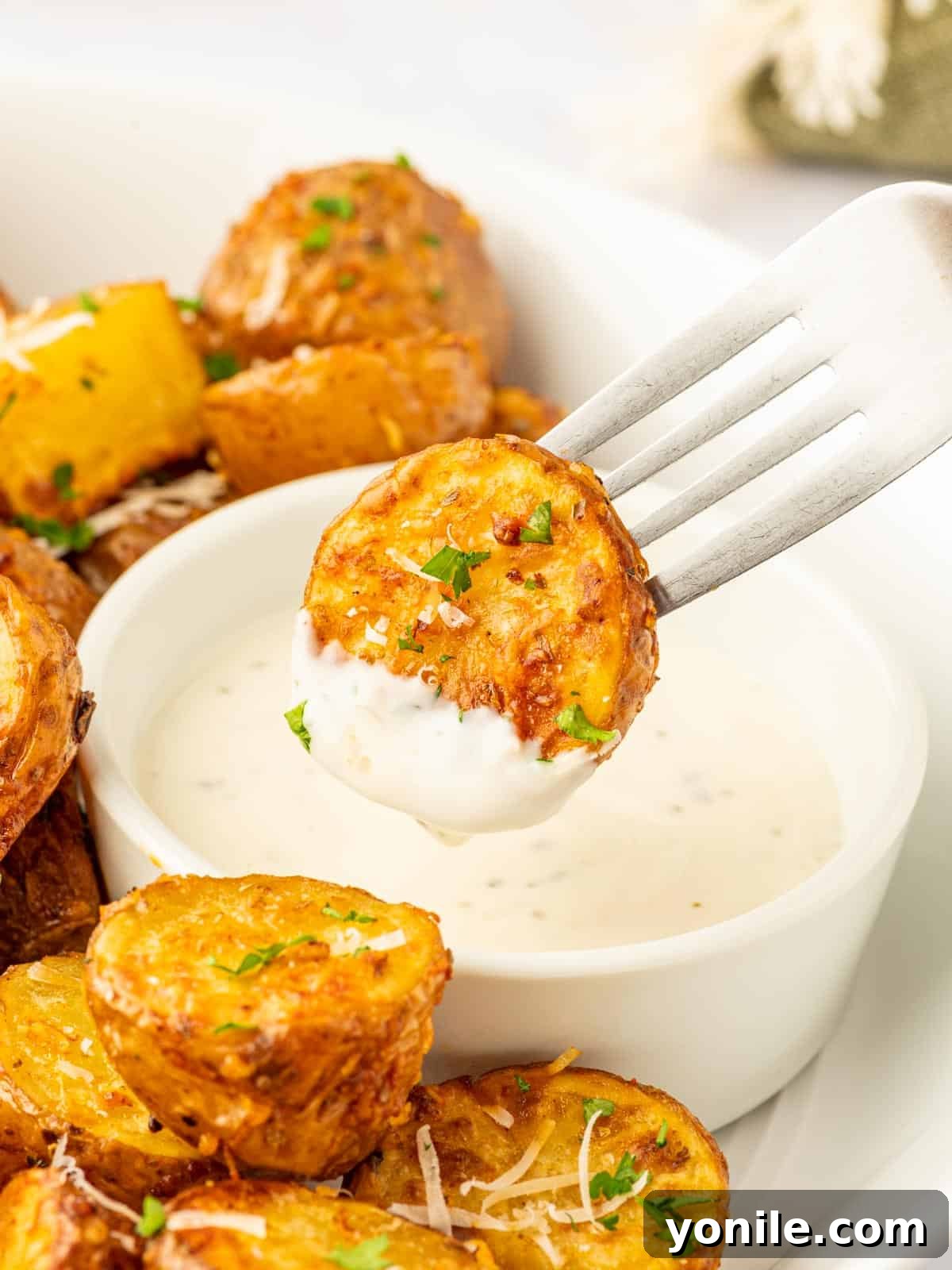 A fork piercing a crispy, golden-brown air-fried potato half, poised above a creamy dipping sauce, ready to be enjoyed.