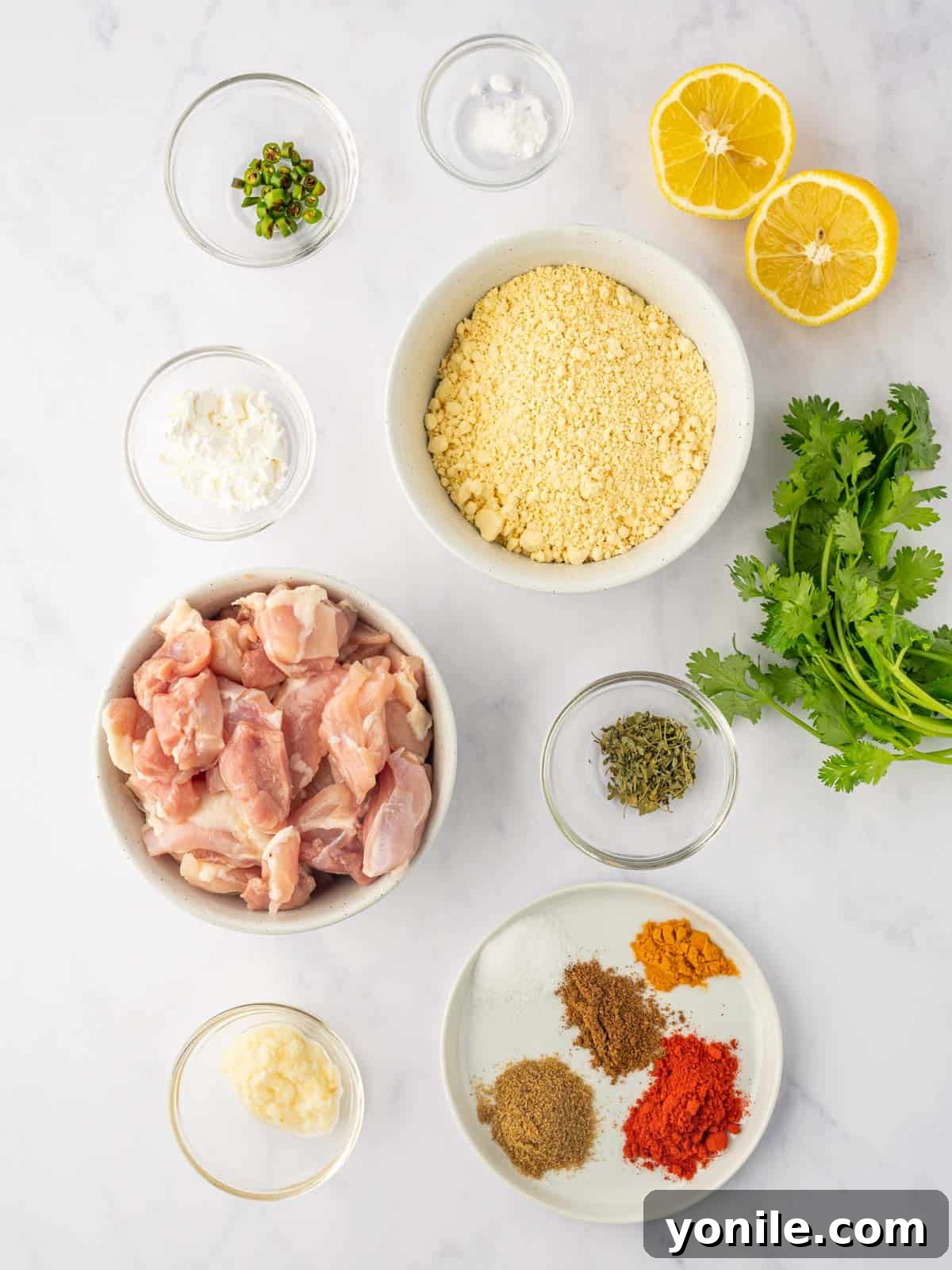 A collection of fresh ingredients laid out, including chicken, lemon, cilantro, and various spices, ready for making chicken pakora.