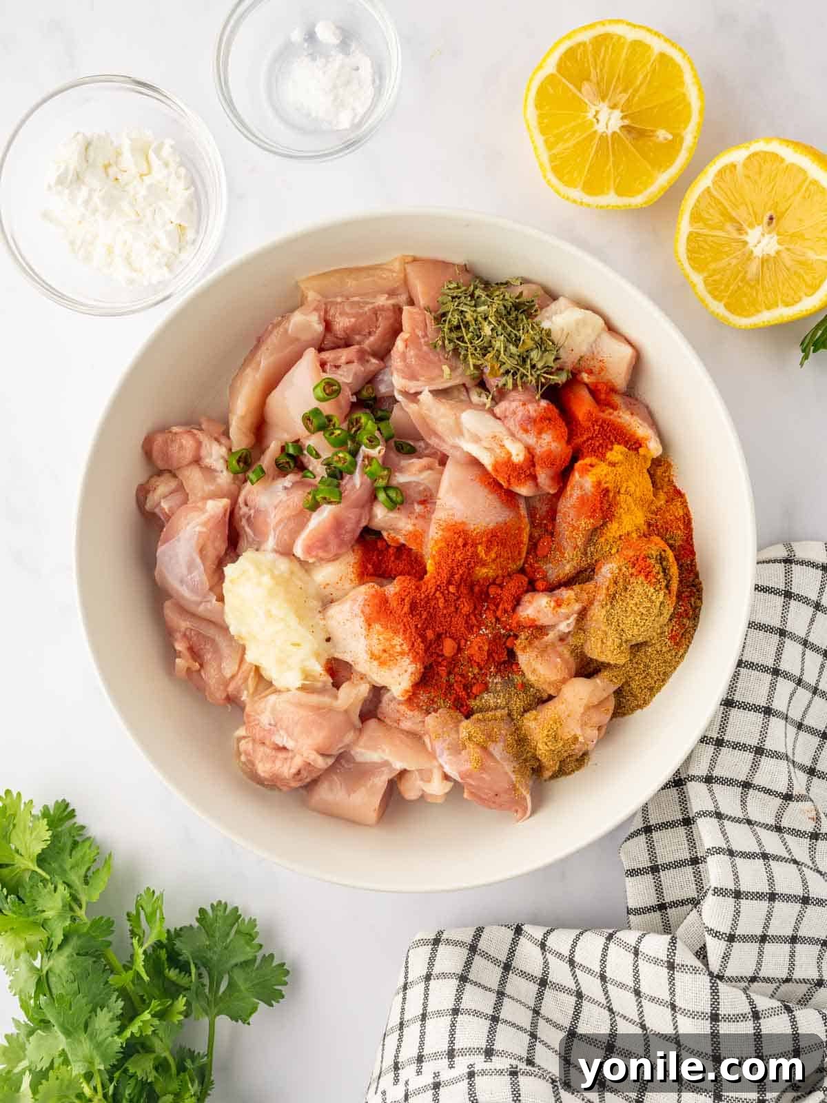 Chicken pieces being seasoned with a vibrant array of spices in a mixing bowl.