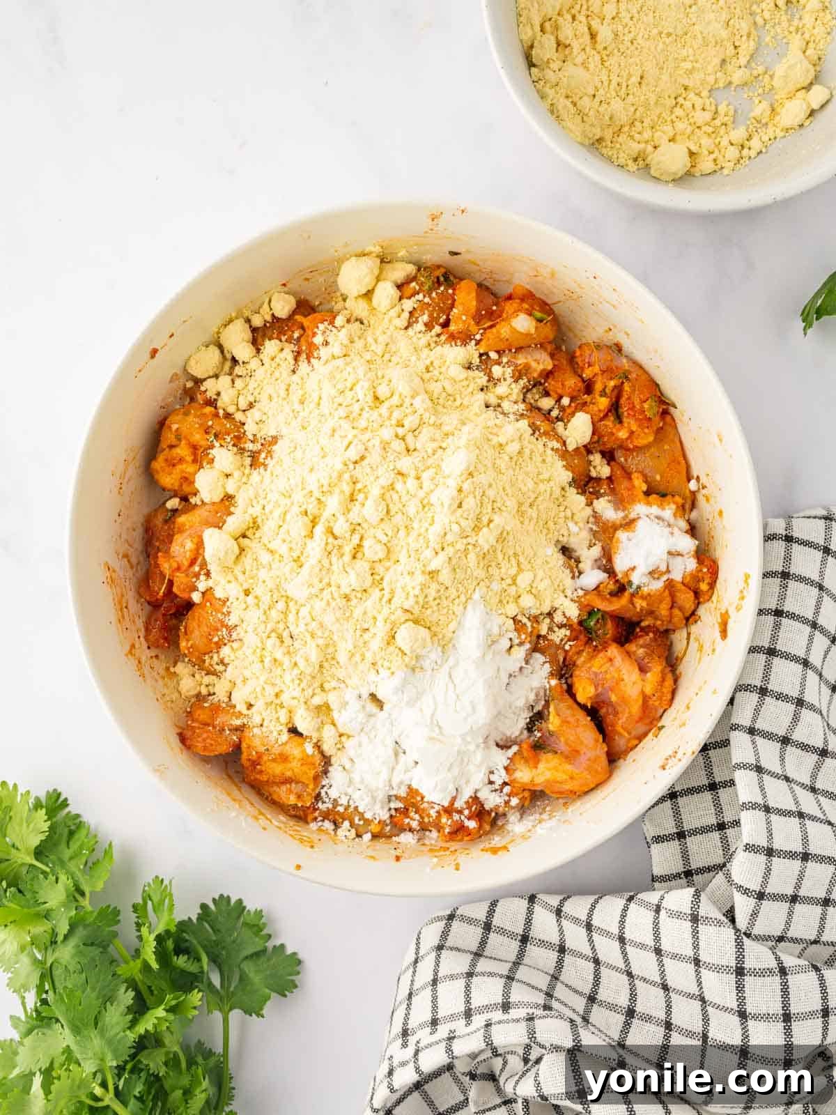Marinated chicken being combined with gram flour and other batter ingredients in a bowl, forming a thick coating.