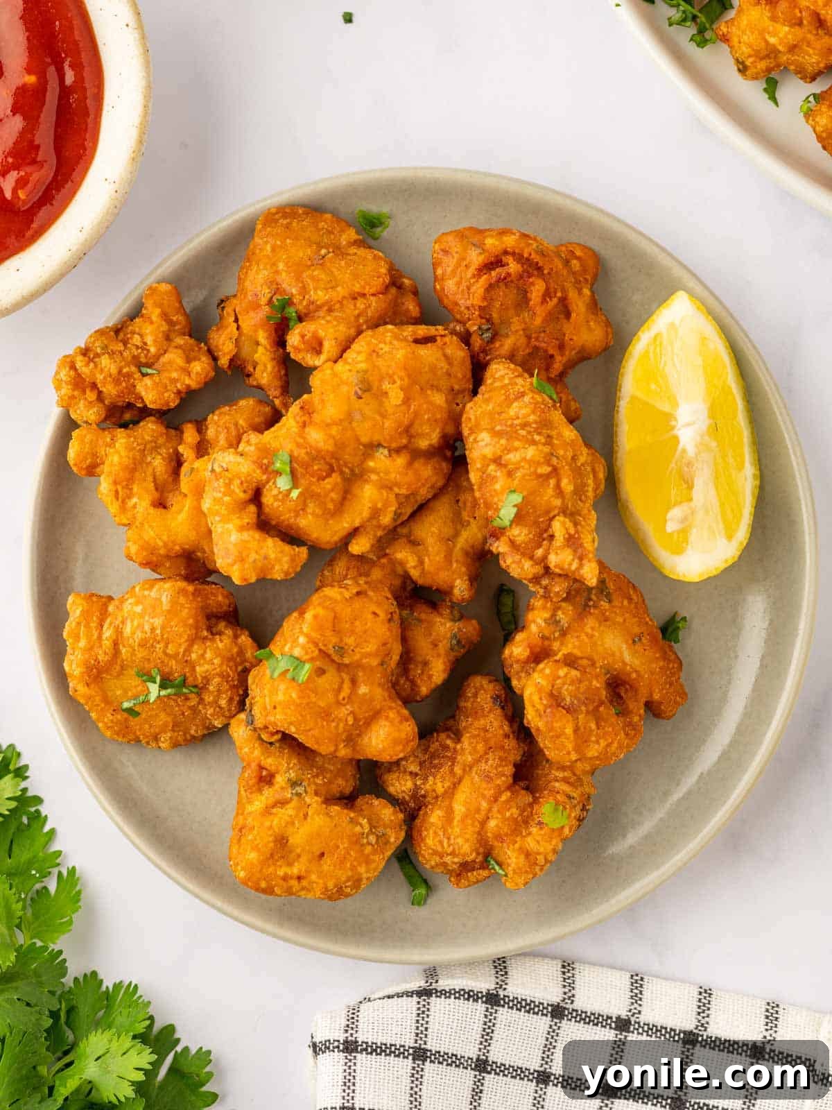 Crispy chicken pakora pieces arranged beautifully on a plate, garnished with a vibrant lemon wedge.