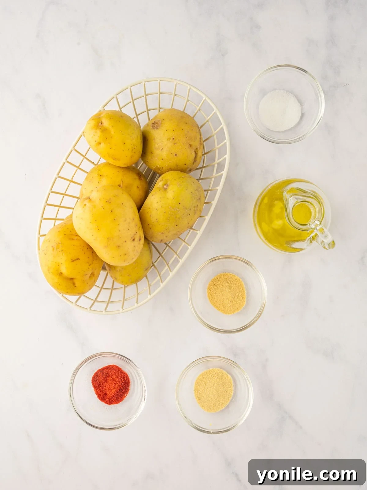 Ingredients for crispy air fryer sliced potatoes including whole Yukon Gold potatoes, a bottle of olive oil, and small bowls of various spices.