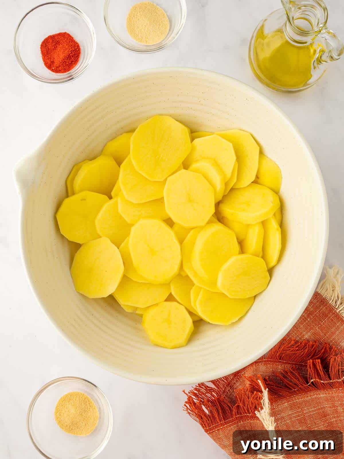 Thin, uniform slices of potato in a bowl, perfectly cut and ready for seasoning.