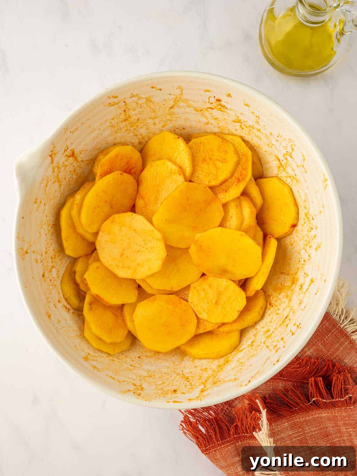 Sliced potatoes being tossed vigorously with seasoning and olive oil until every piece is well coated.