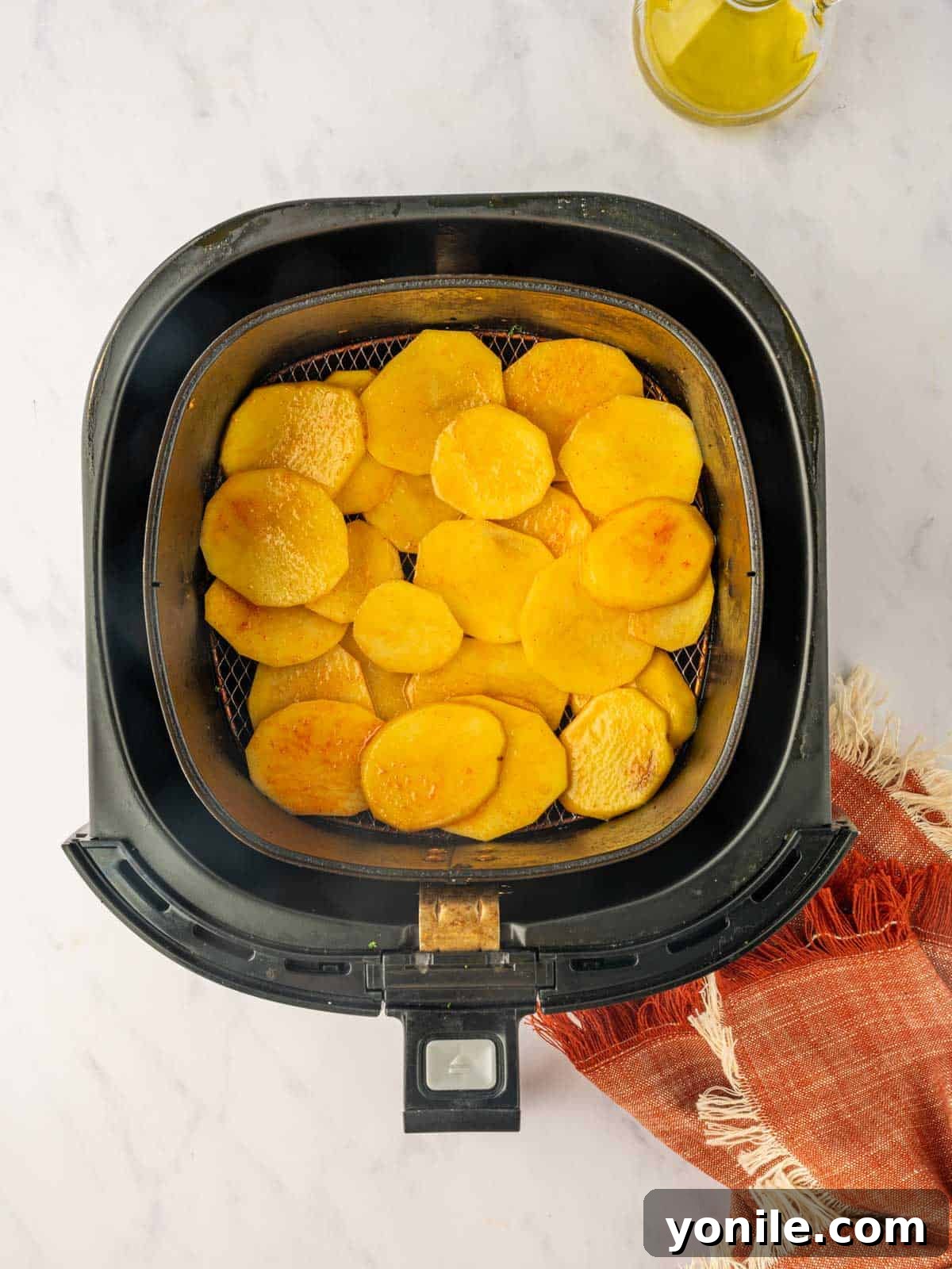 Seasoned potatoes being carefully layered in an air fryer basket in a single layer.