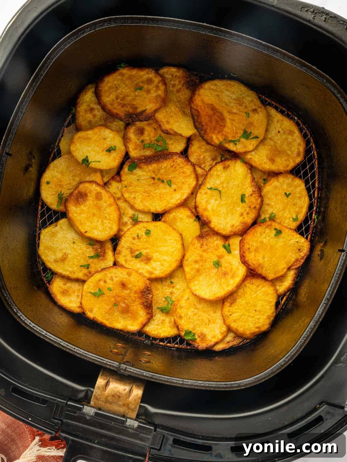 Crispy sliced potatoes in the air fryer, garnished with fresh parsley on a white serving platter.