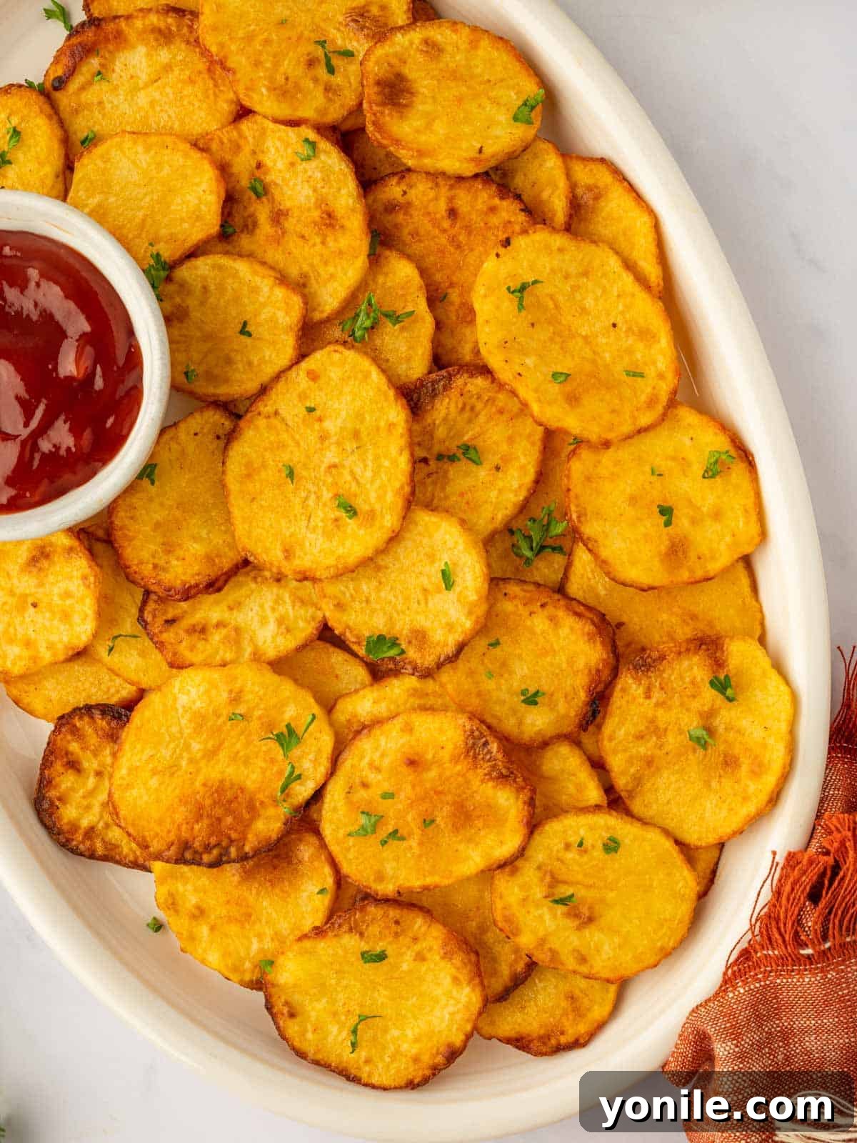 A large platter of golden, crispy air-fried potato chips piled high, with a small bowl of ketchup for dipping.