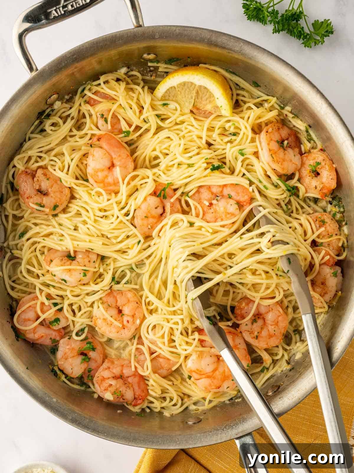Tongs lift a portion of angel hair pasta from a skillet.