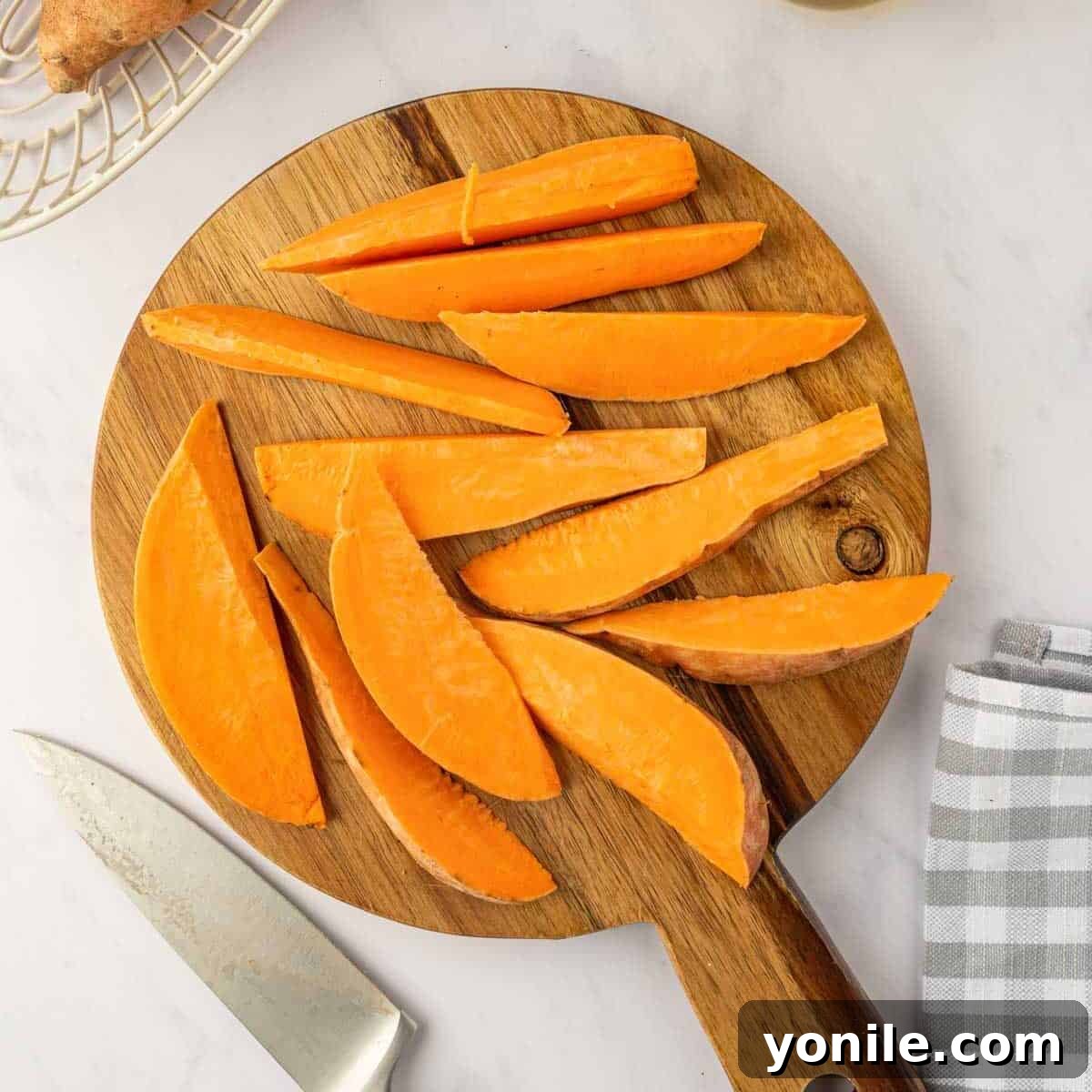 A sweet potato being expertly sliced into uniform wedges on a sturdy cutting board, demonstrating the correct cutting technique.