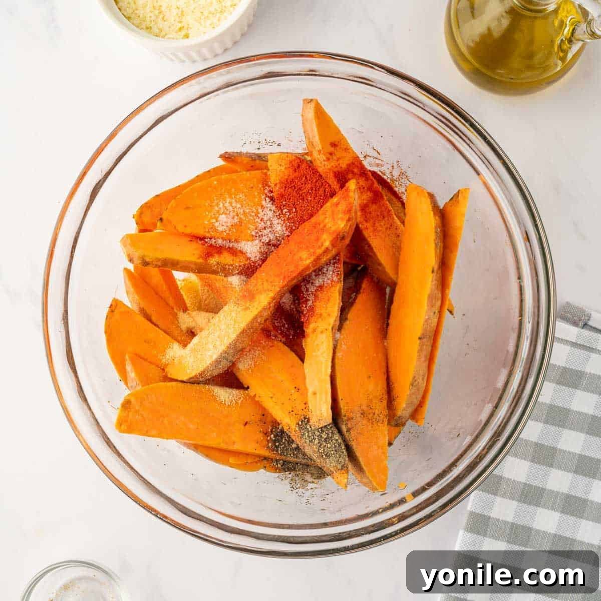 Sliced sweet potato wedges being vigorously tossed with olive oil and a medley of savory spices in a spacious mixing bowl, ensuring every piece is coated.