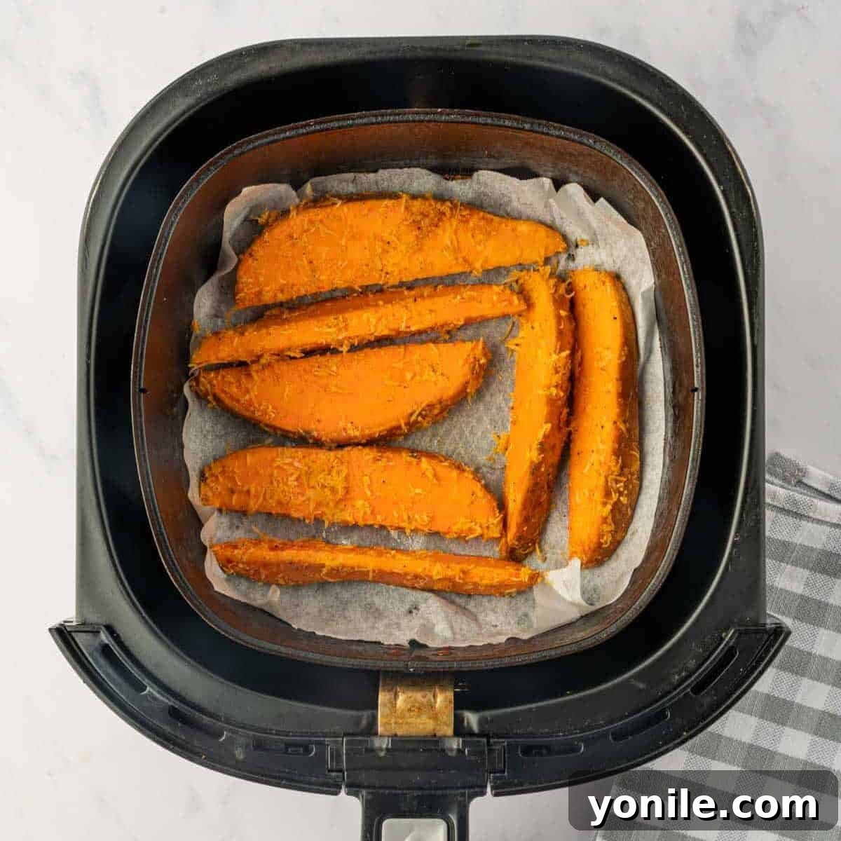 Parmesan-coated sweet potato wedges being meticulously arranged in an air fryer basket in a single, uncrowded layer, ready for cooking.
