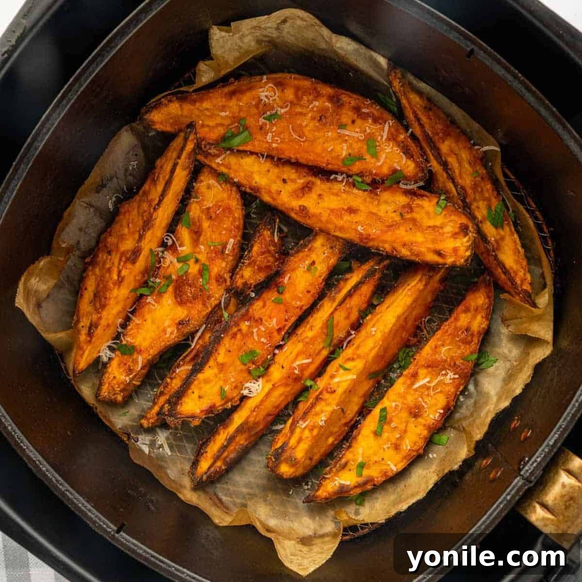 A close-up view of perfectly cooked, golden-brown, crispy air-fried sweet potato wedges resting beautifully in the air fryer basket after completion.