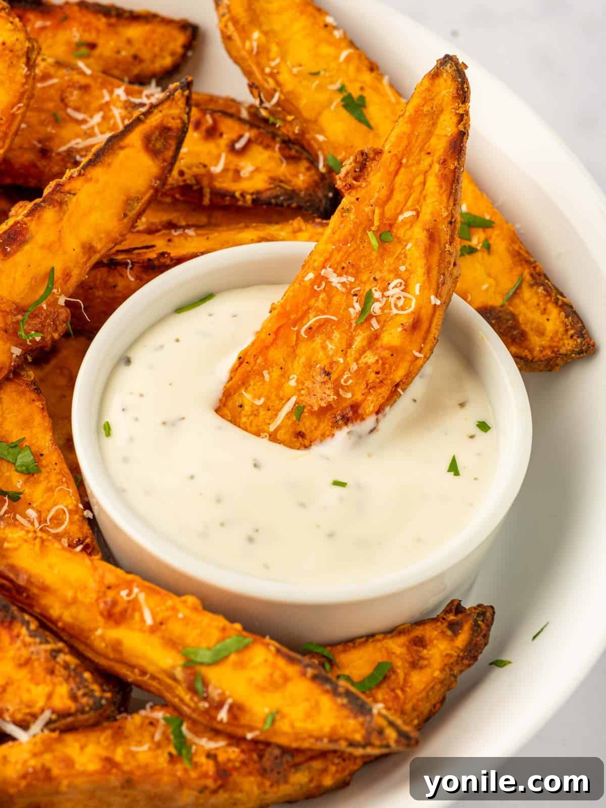 A crispy sweet potato wedge being gracefully dipped into a small dish of creamy sauce, artfully highlighting its perfect golden texture and inviting appeal.