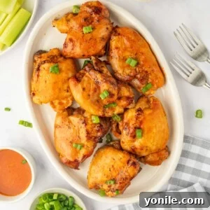 A platter of baked chicken thighs basted with buffalo sauce, garnished with fresh herbs.