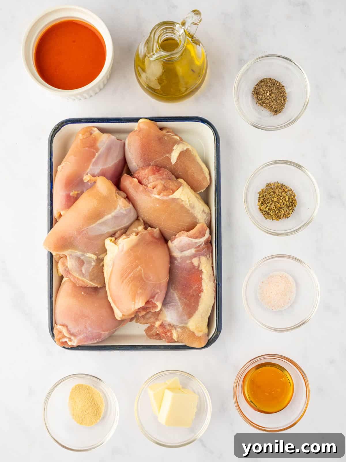 Various ingredients for baked buffalo chicken thighs including chicken, spices, hot sauce, butter, and honey.